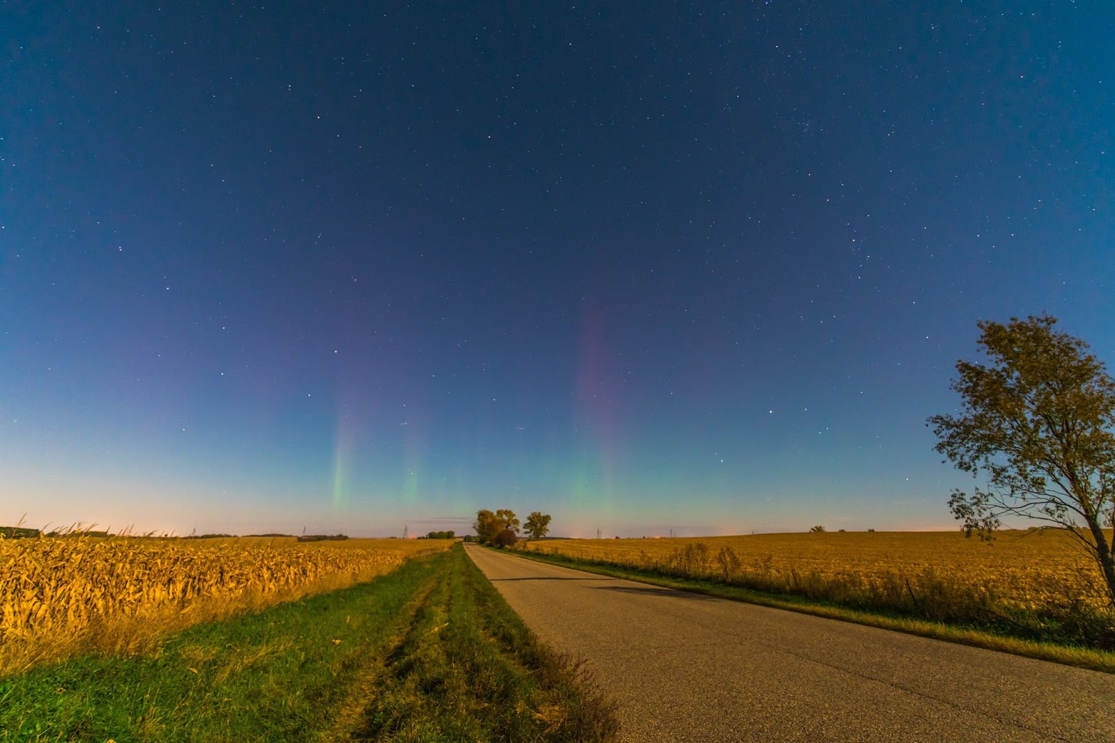 A colorful photo of a flat landscape shows faint green and red aurora pillars