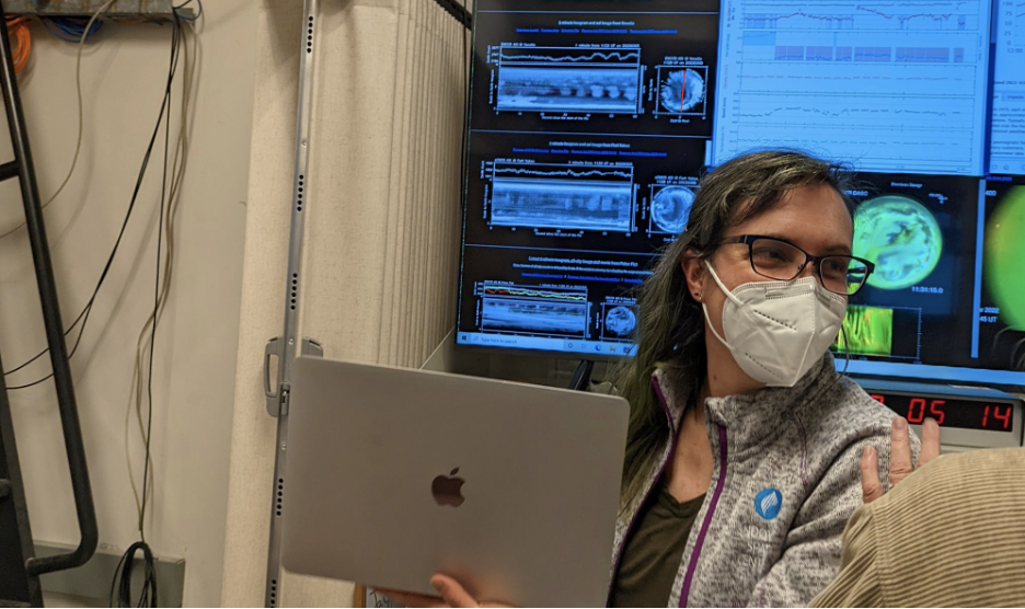 A woman in an N95 style mask holds a laptop
