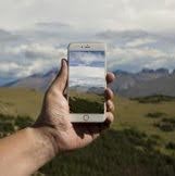 Image of a hand holding a smartphone with GLOBE Observer on it up against a landscape