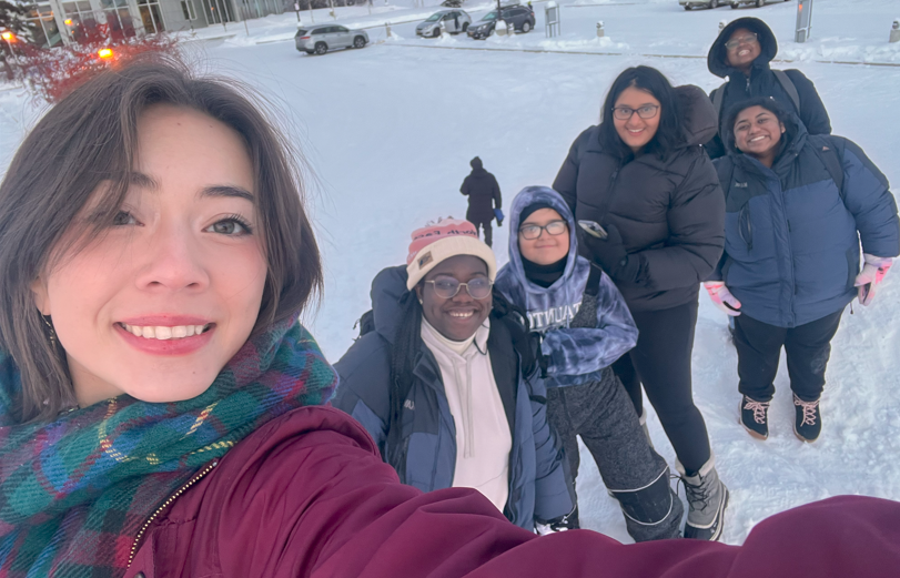 Six smiling students stand in the snow.