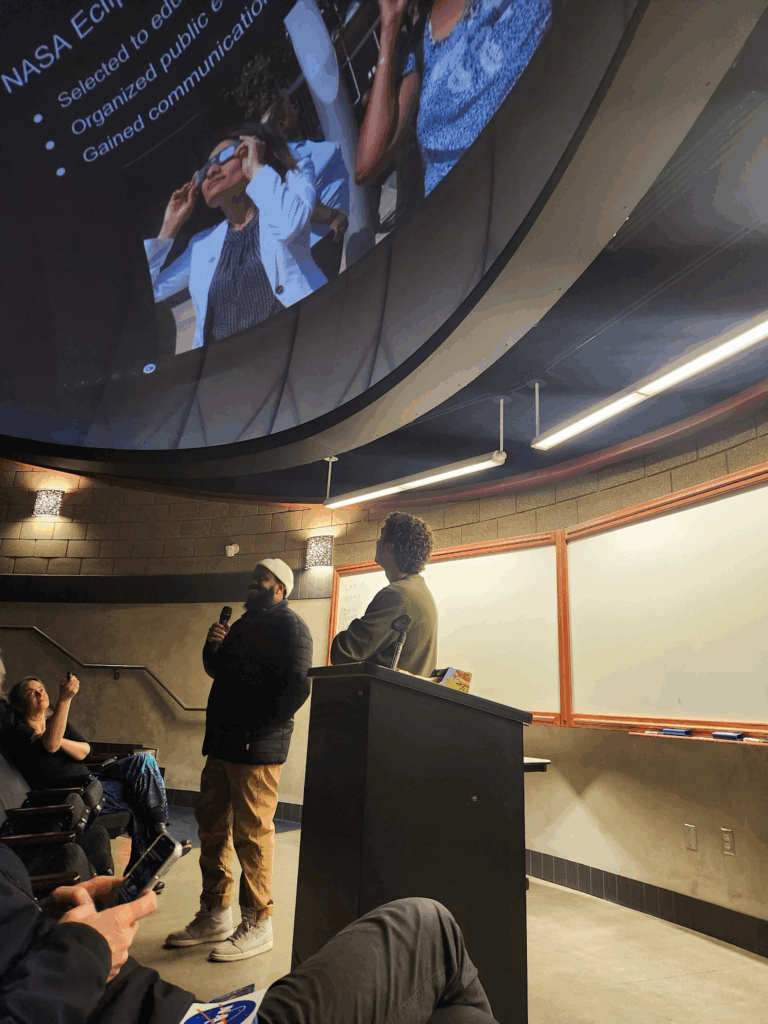 A young man stands beneath a planetarium screen, giving an engaging presentation.