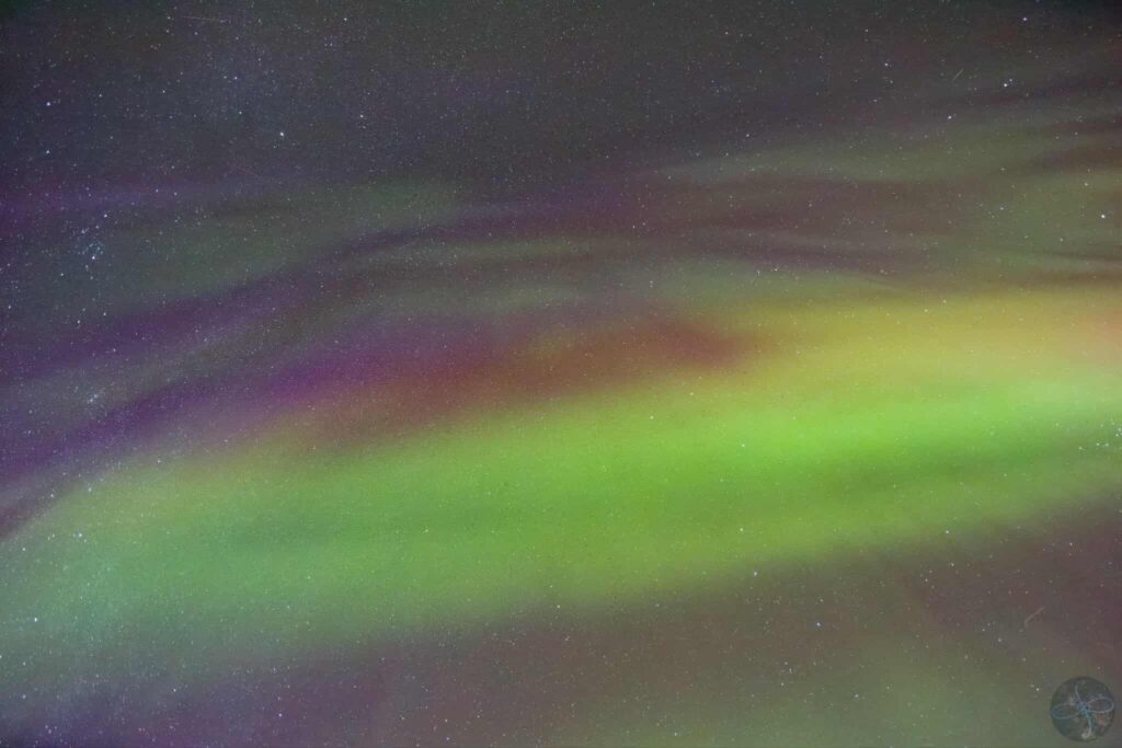 The viewer looks up into a sheetlike beautiful aurora with red, green, blue, purple, and yellow hues.