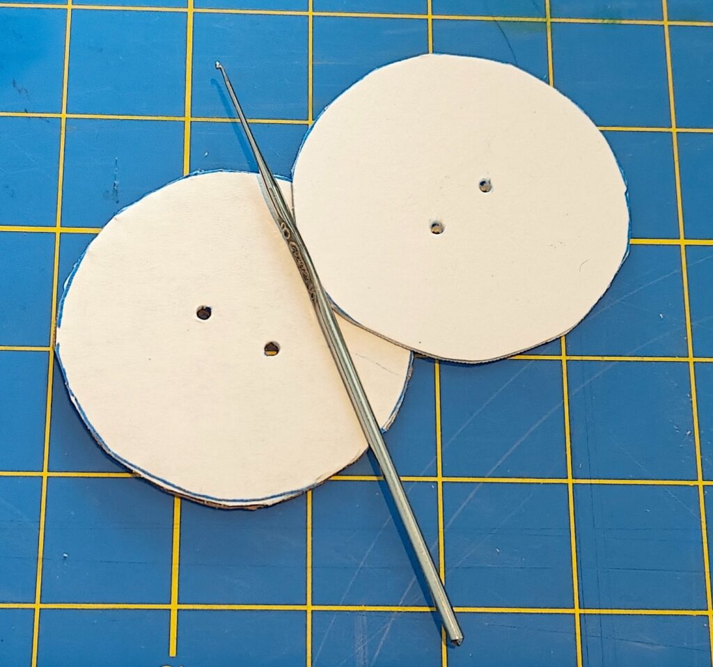 Image shows cardboard and quickboard circles with holes poked in them, with a small crochet hook