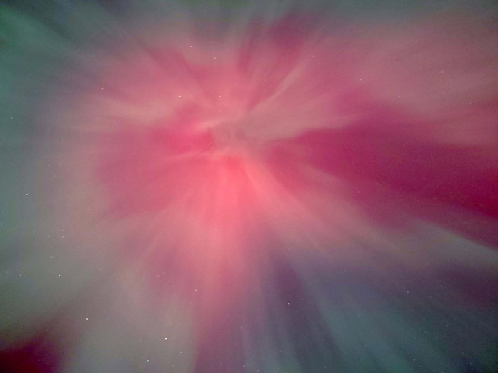 Aurora blossoms from the center of this overhead photo like a red and pale green starburst