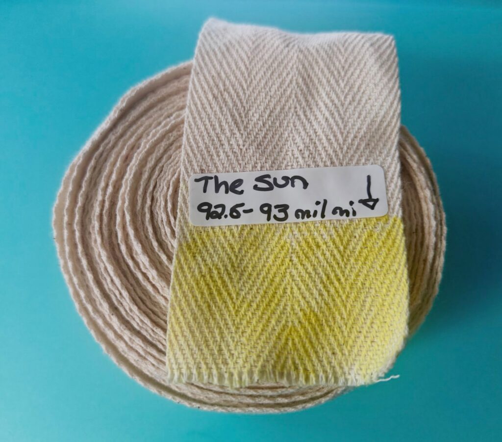 A roll of twill tape. The end lies on top of the roll, with the last inch and a half colored yellow and labeled The Sun
